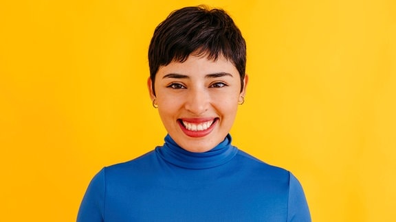 Portrait einer jungen, lächelnden Frau vor knallgelbem Hintergrund