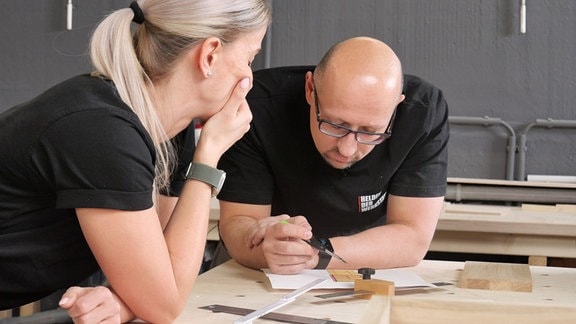 Ein Mann und eine Frau spechen in einer Werkstatt über eine Bauanleitung.