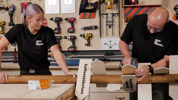 Ein Mann und eine Frau bauen an einem Wegweiser in einer Werkstatt.