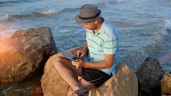 Mann arbeitet an seinem Tablet am Strand.