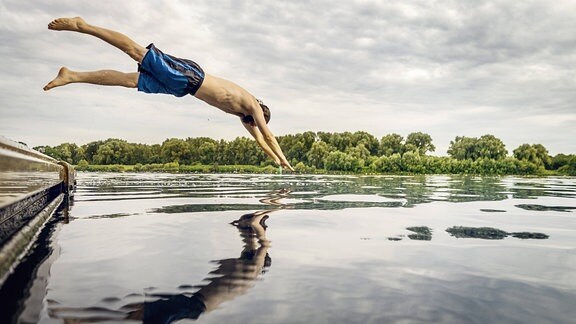 Junger Mann springt von einem Steg in einen See.
