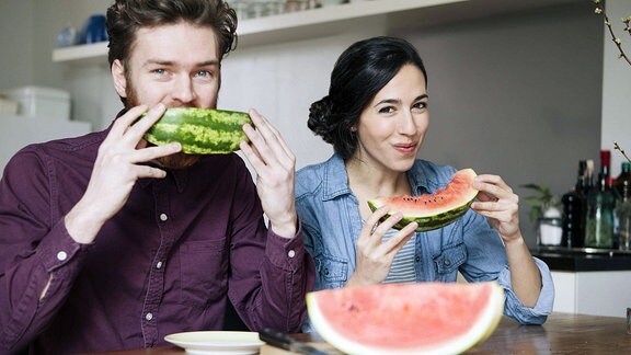 Ein junges Paar genießt am Küchentisch sitzend  Wassermelone.