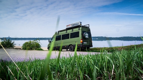 Ein grüner Camper steht auf einem Parkplatz am Cospudener See.