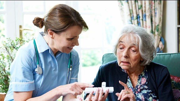 Eine junge Pflegerin gibt einer älteren Frau Hinweise zur Tabletteneinnahme.