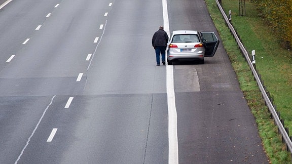 Autopanne - Ein Mann steht neben seinem Wagen auf dem Standstreifen einer Autobahn.