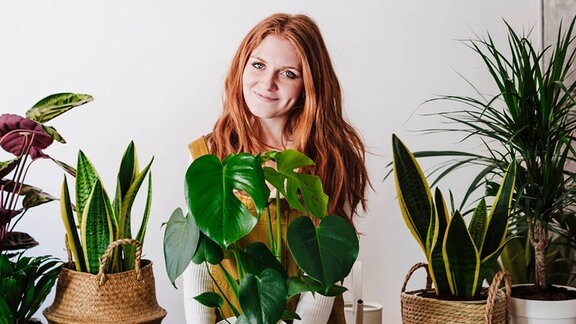 Eine Frau zeigt Zimmerpflanzen und hält dabei eine Monstera.