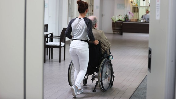 Vorstellung Besuchszimmer in städtischen Pflegeeinrichtungen. Eine Pflegerin schiebt einen alten Mann im Rollstuhl.
