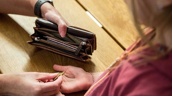 Ein Kind bekommt von der Mutter, die eine Geldbörse in den Händen hält, Ihr Taschengeld auf die Hand.