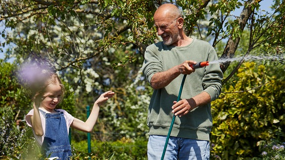 Ein Mann mit einem Gartenschlauch in einem grünen Garten