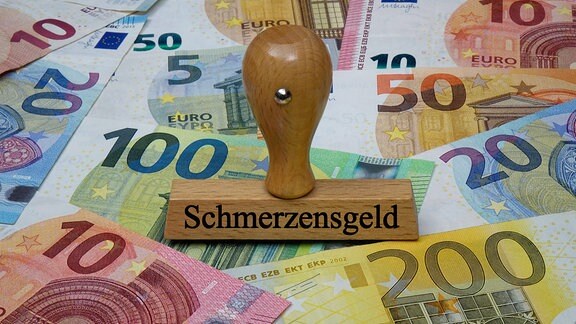 Geldscheine und Stempel mit Aufdruck "Schmerzensgeld"