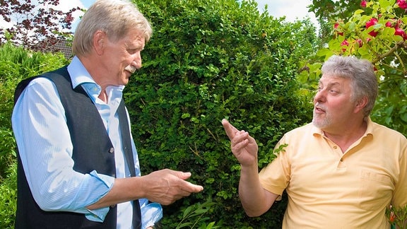 Zwei Männer vor einer Hecke