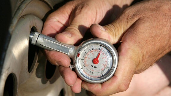 Mann prüft mit einem Luftdruckmesser den Druck auf einen Reifen