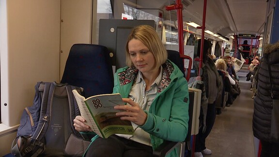 Reporterin Juliane Zeisler sitzt mit einem Kursbuch von 1989/90 in einem Zug.