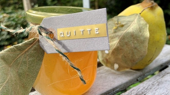 Ein Glas mit Gelee steht neben einer Quitte.