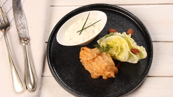 Auf einem Teller sind panierter Fisch, Salat und ein Dip arrangiert.