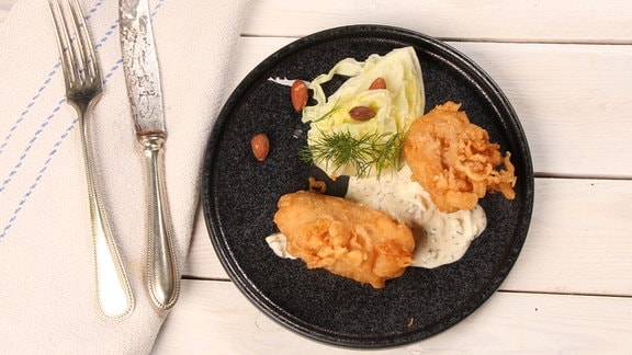 Auf einem Teller sind panierter Fisch, Salat und ein Dip arrangiert.