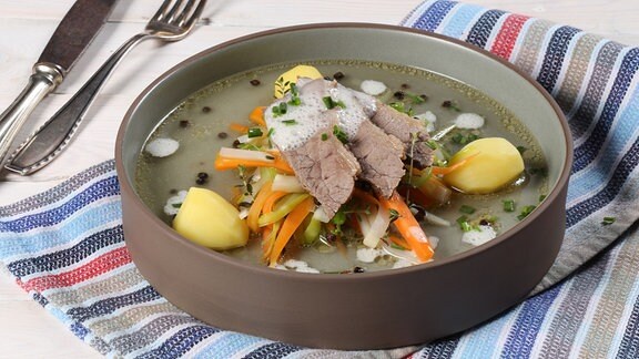 Suppe und Fleisch angerichtet auf einem tiefen Teller.