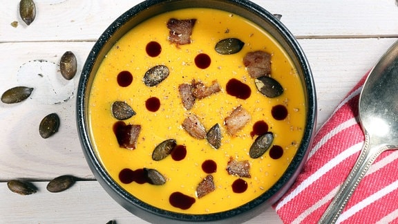 Sonnengelbe Suppe in einer runden Schale, garniert mit Kürbiskernen und Öl.