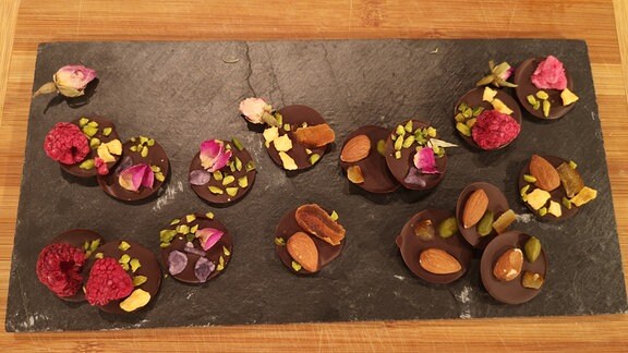 Mendiants mit Blüten, Früchten und Mandeln auf einer Schieferplatte