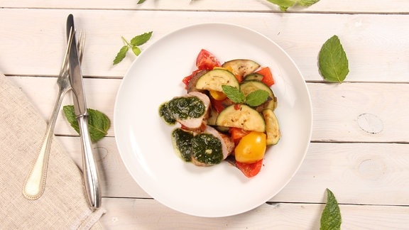 Auf einem Teller sind Gemüse und Schweinefilets attraktiv arrangiert.