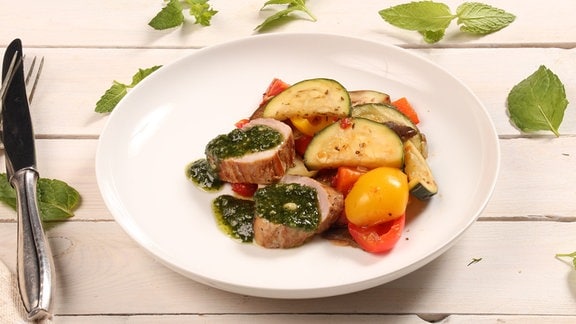Auf einem Teller sind Gemüse und Schweinefilets attraktiv arrangiert.