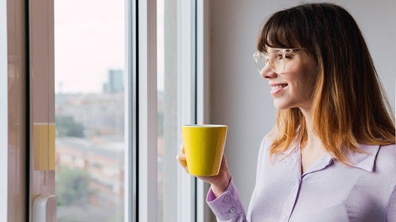 Lächelnde Geschäftsfrau mit Kaffeetasse, die durch ein Fenster schaut