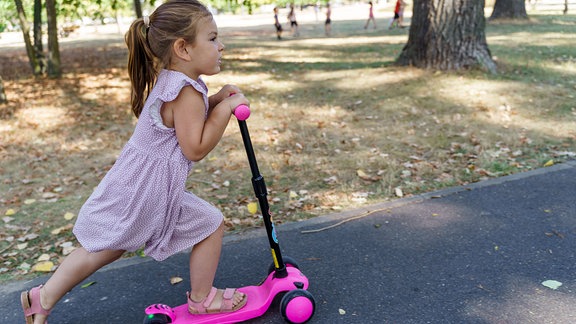 Mädchen fährt Tretroller im Park.
