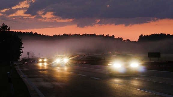 Verkehr auf der Autobahn bei Sonnenuntergang und einem Nebelfeld.