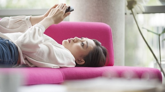 Frau liegt auf Sofa und schaut aufs Smartphone