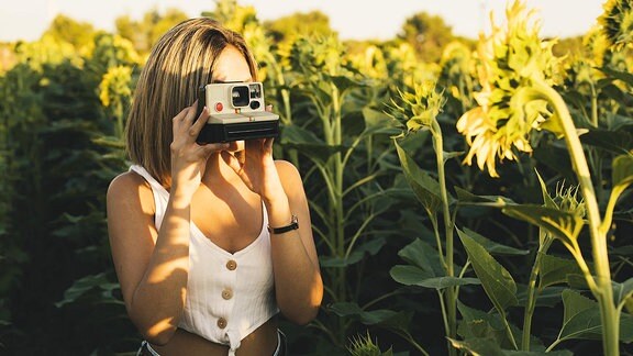 Junge Frau fotografiert mit einer Sofortbildkamera.