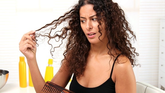 Eine junge Frau kämmt ihre lockigen Haare.