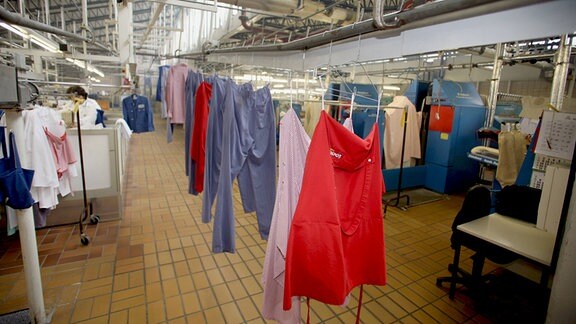 Kittel, Hemden und Hosen hängen gereinigt auf Bügeln in einer Großwäscherei.