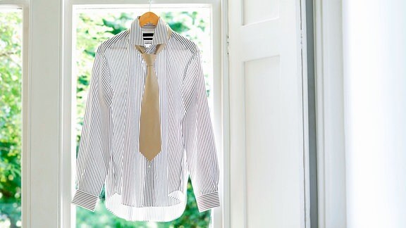 Ein frisches Hemd hängt auf einem Bügel vor einem Fenster.