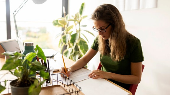 Eine Frau arbeitet an einem Schreibtisch, umgeben von Zimmerpflanzen