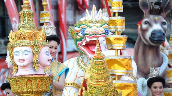 Eine Frau schaut lächelnd hinter einer Buddhastatue hervor