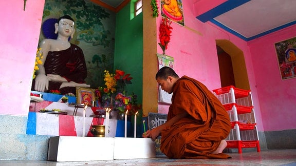 Ein Mönch zündet vor einer Buddha-Statue Kerzen an