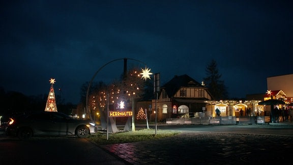 Mehrere Häuser, die weihnachtlich erleuchtet sind, davor ein Herrnhuter Stern mit 25 Zacken.