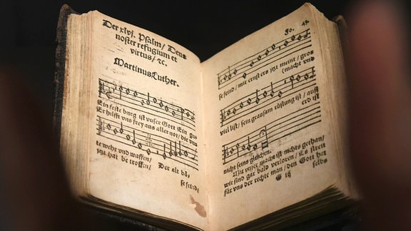 Ein Gemeindegesangbuch einer zweiten Auflage des "Klug,sches Gesangbuch" liegt hinter einer Hand in einer Glasvitrine im Augusteum in der Lutherstadt Wittenberg.