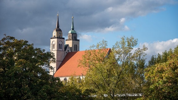 Eine Kirche ragt vor dunklen Wolken hinter Baumwipflen hervor.