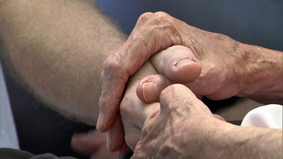 Händepaar einer älteren Person umfasst eine weitere Hand.
