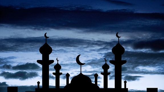 Minarette einer Moschee zeichnen sich als Schatten vor einem dunklen Himmel mit Halbmond ab.
