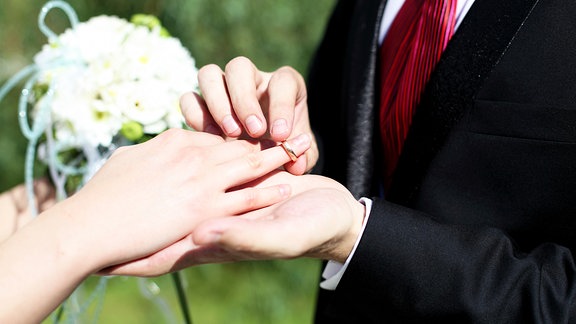 Ein Bräutigam steckt einer Braut einen Ring an den Finger