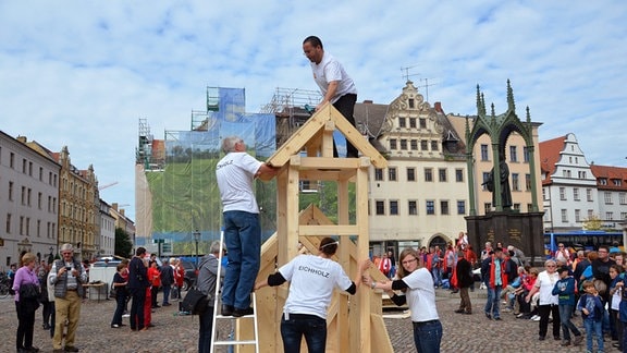 Menschen bauen eine Kirche im Miniformat aus Holzteilen