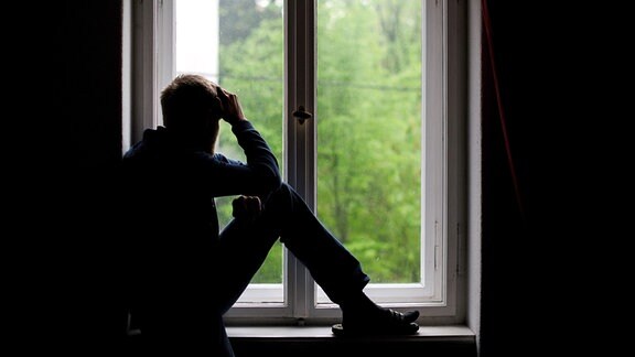 Ein Mann sitzt allein in einem Fenster und schaut nach draußen.