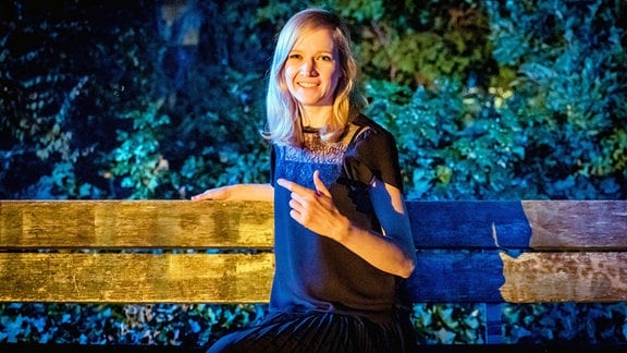 Blonde Frau (Clarissa Herzog) sitzt im Dunklen auf einer Parkbank.