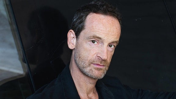 Schauspieler Jörg Hartmann vor dunklem Hintergrund.