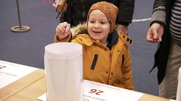 Ein Junge lacht freudig als er einen "Stimm Taler" in eine Wahlurne legen kann.