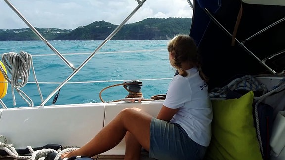 Junge Frau sitzt an der Reling eines Bootes und schaut zum Festland.