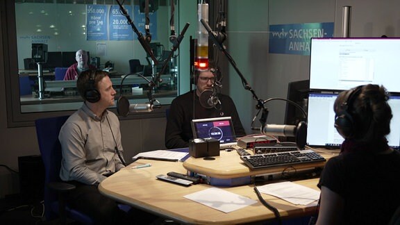 Drei Personen in einem Radiostudio, sprechen während einer Sendung miteinander.