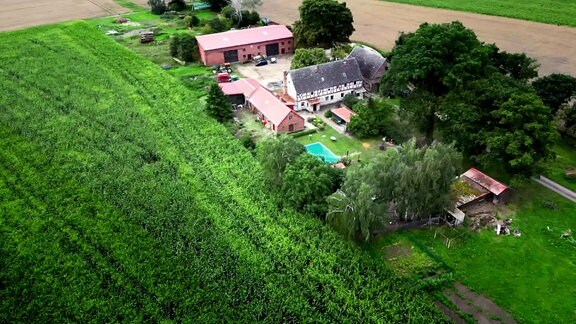 Luftbildaufnahme zeigt einen Bauernhof umgeben von Wiesen und Feldern.